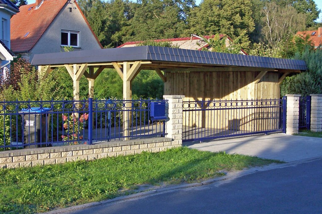 Maßgefertigter Holzcarport mit integriertem Abstellraum und dunkler Blende vor einem Wohnhaus
