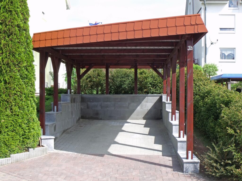 Massgefertigter Holzcarport mit roter Schindelblende und gemauerter Stützwand