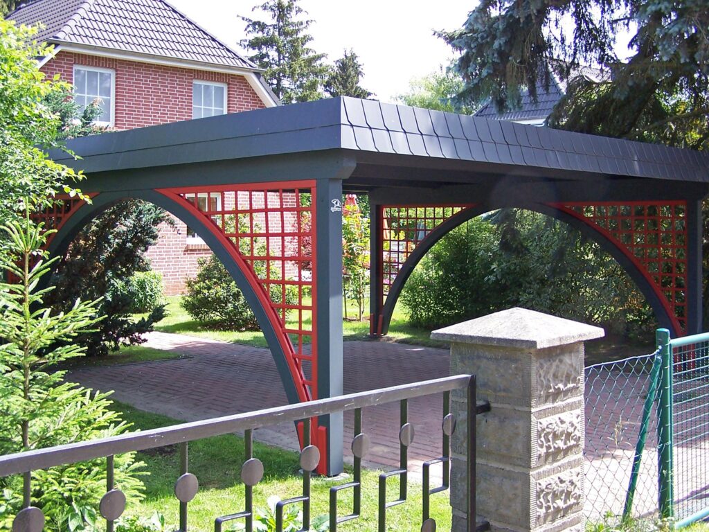 Moderner Rundbogen-Carport in Anthrazit und Rot auf einer gepflasterten Einfahrt vor einem Wohnhaus
