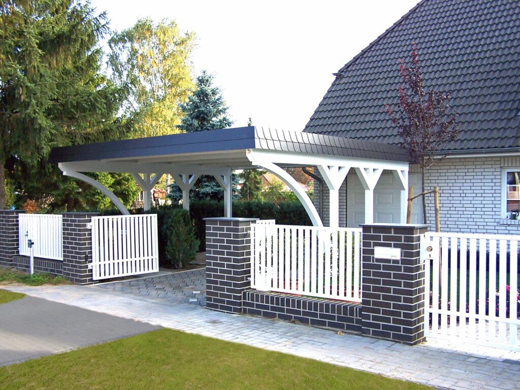 Weißer Rundbogen-Carport aus Holz vor einem Einfamilienhaus mit dunklem Ziegeldach