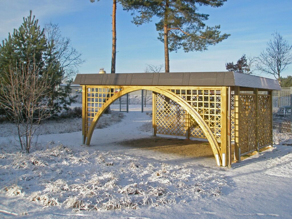 Bogengang-Carport aus Holz mit Rankgitter-Elementen in verschneiter Umgebung