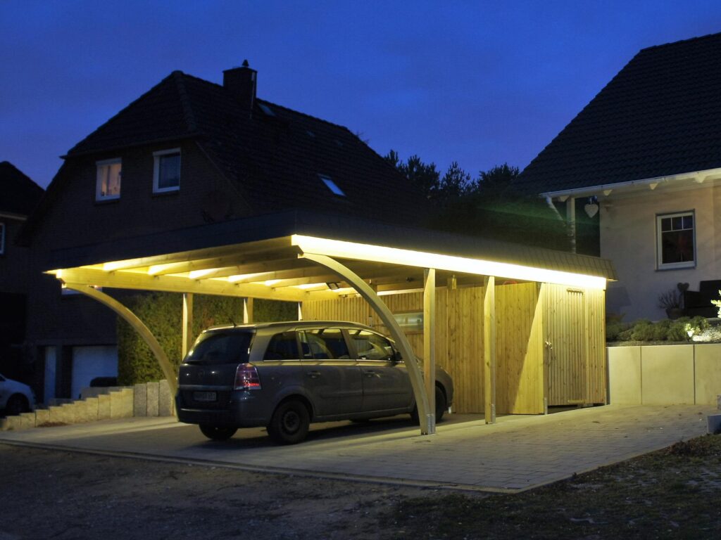 Rundbogen-Carport aus Holz mit integriertem Geräteraum und Beleuchtung bei Nacht