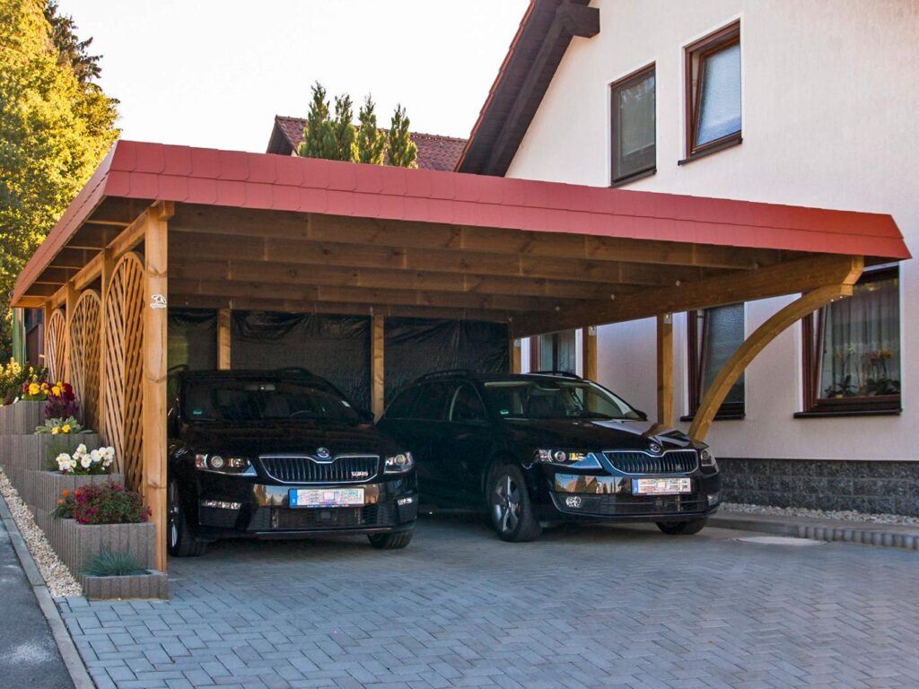 Rundbogen-Carport aus Holz mit roter Schindelblende schützt zwei Autos