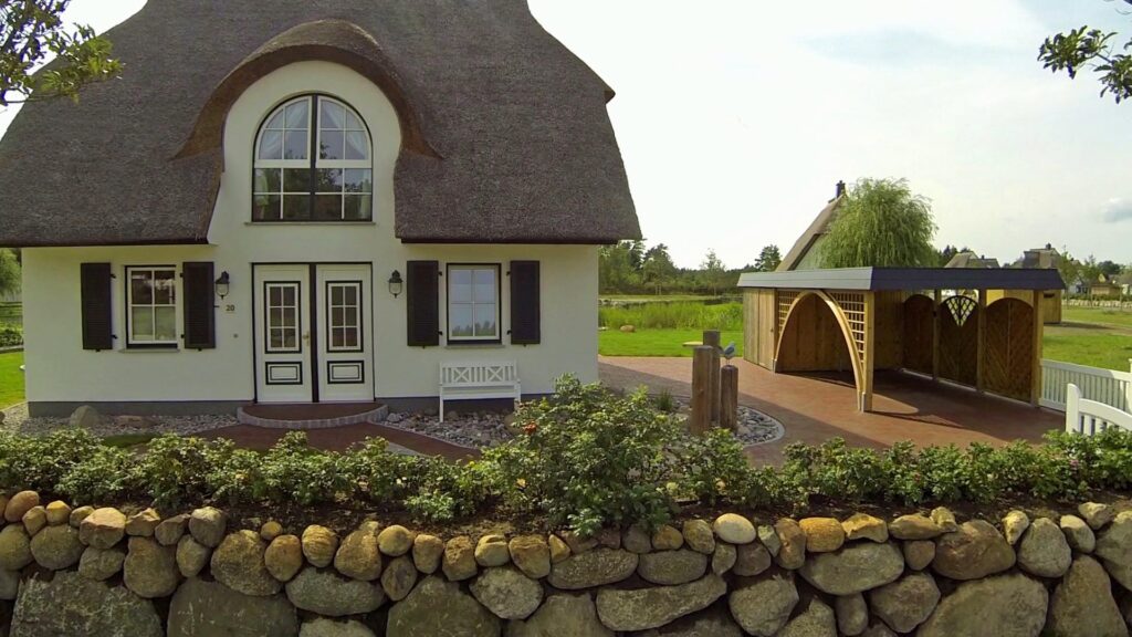 Rundbogen-Einzelcarport mit Bogengang und Abstellkammer neben einem Haus mit Reetdach